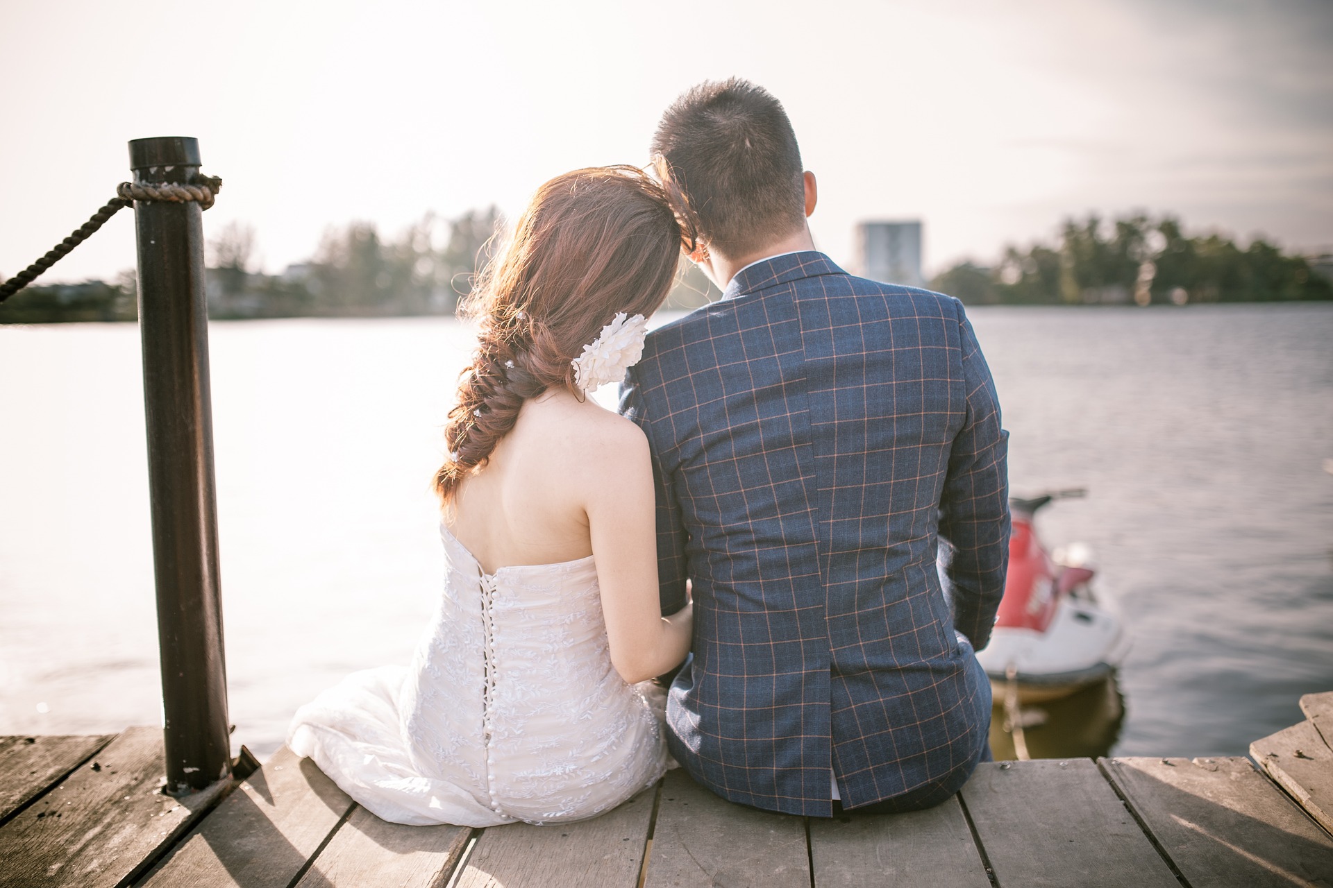 Na obrázku je mladý pár svatebčanů sedící na molu u vody